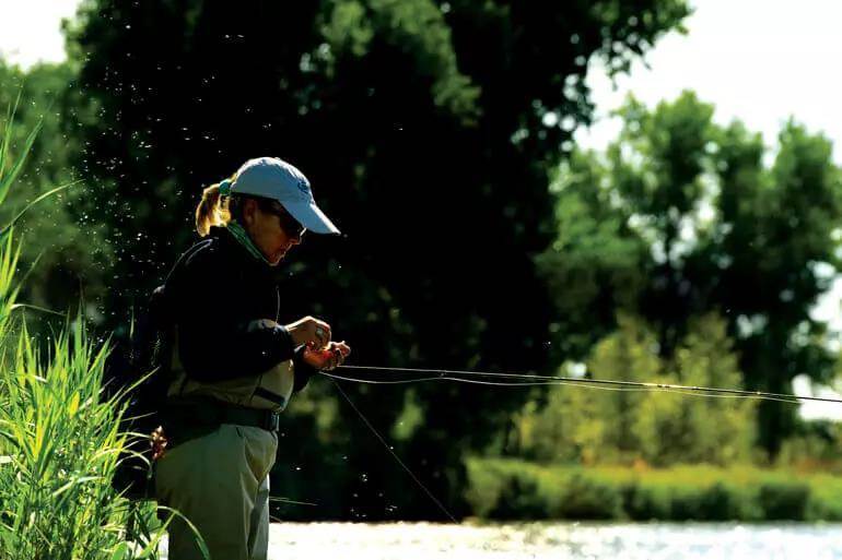 A fly angler dressing a dry fly below clouds of mayflies. 