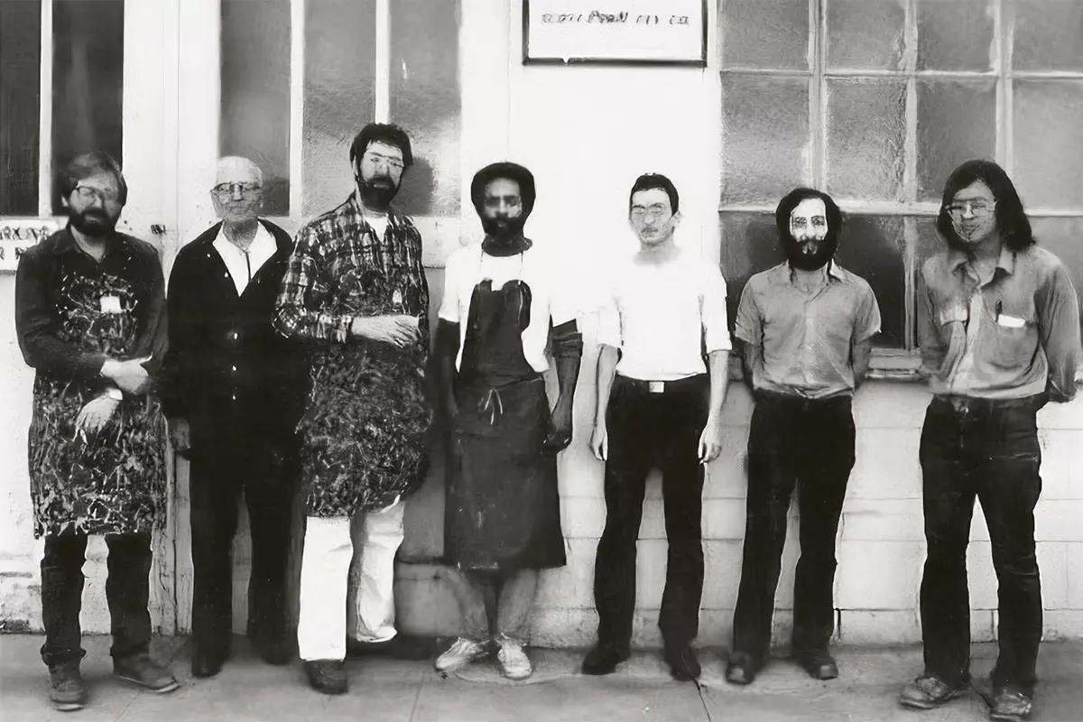 Seven men in aprons standing outside of a building. 