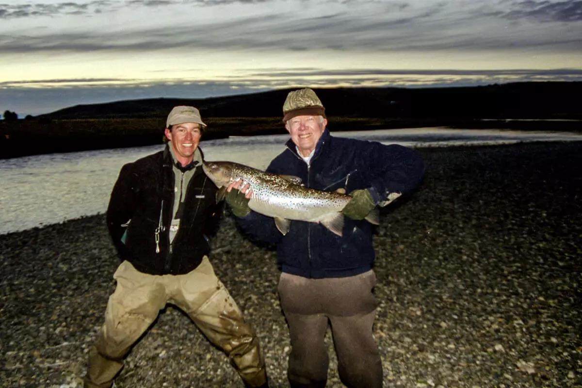 Former President Jimmy Carter holding a huge Argentine brown trout with his guide, at sunset.