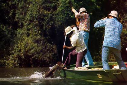 An old photo of a fly angler in a small jon boat fighting a tarpon while his guide gaffs it.