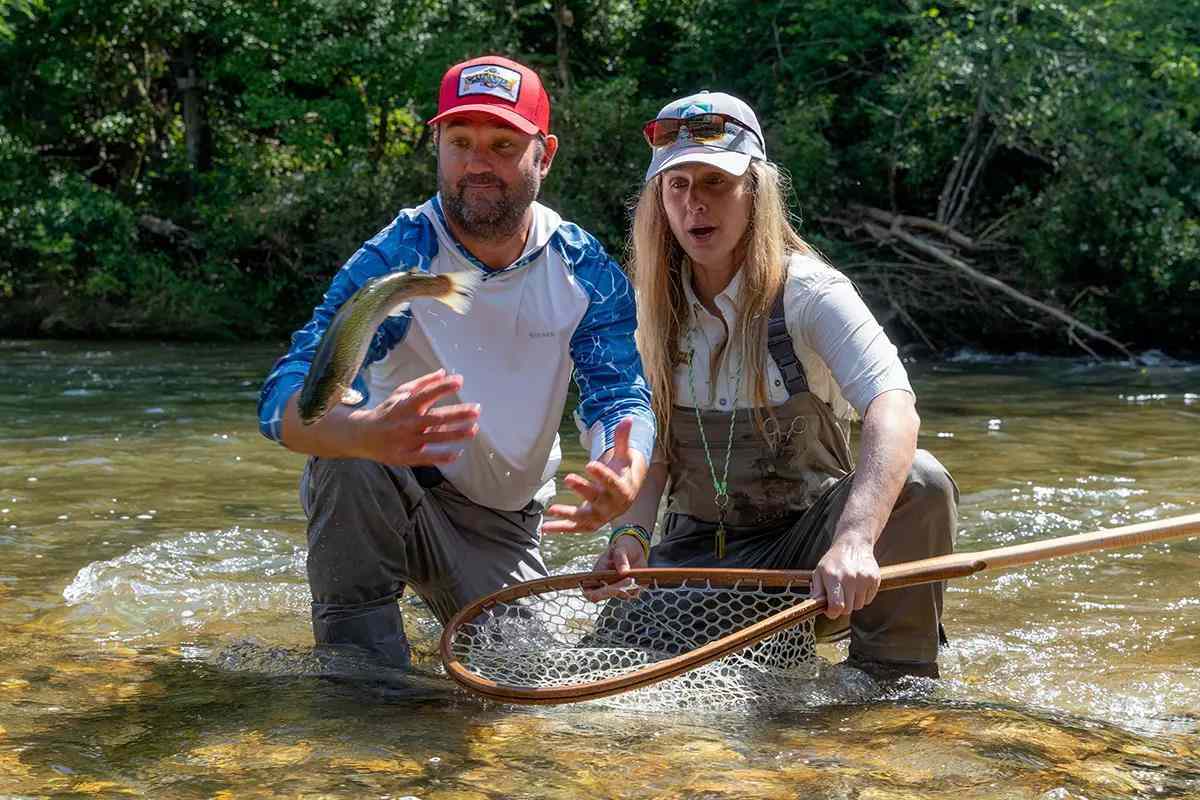A man and a woman kneeling in a river for a grip-n-grin photo with the fish flopping out one's hands.