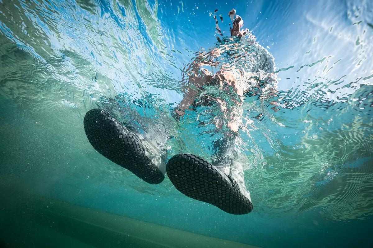 An underwater photo of a wading flats fly angler; the camera is looking up out of the water.
