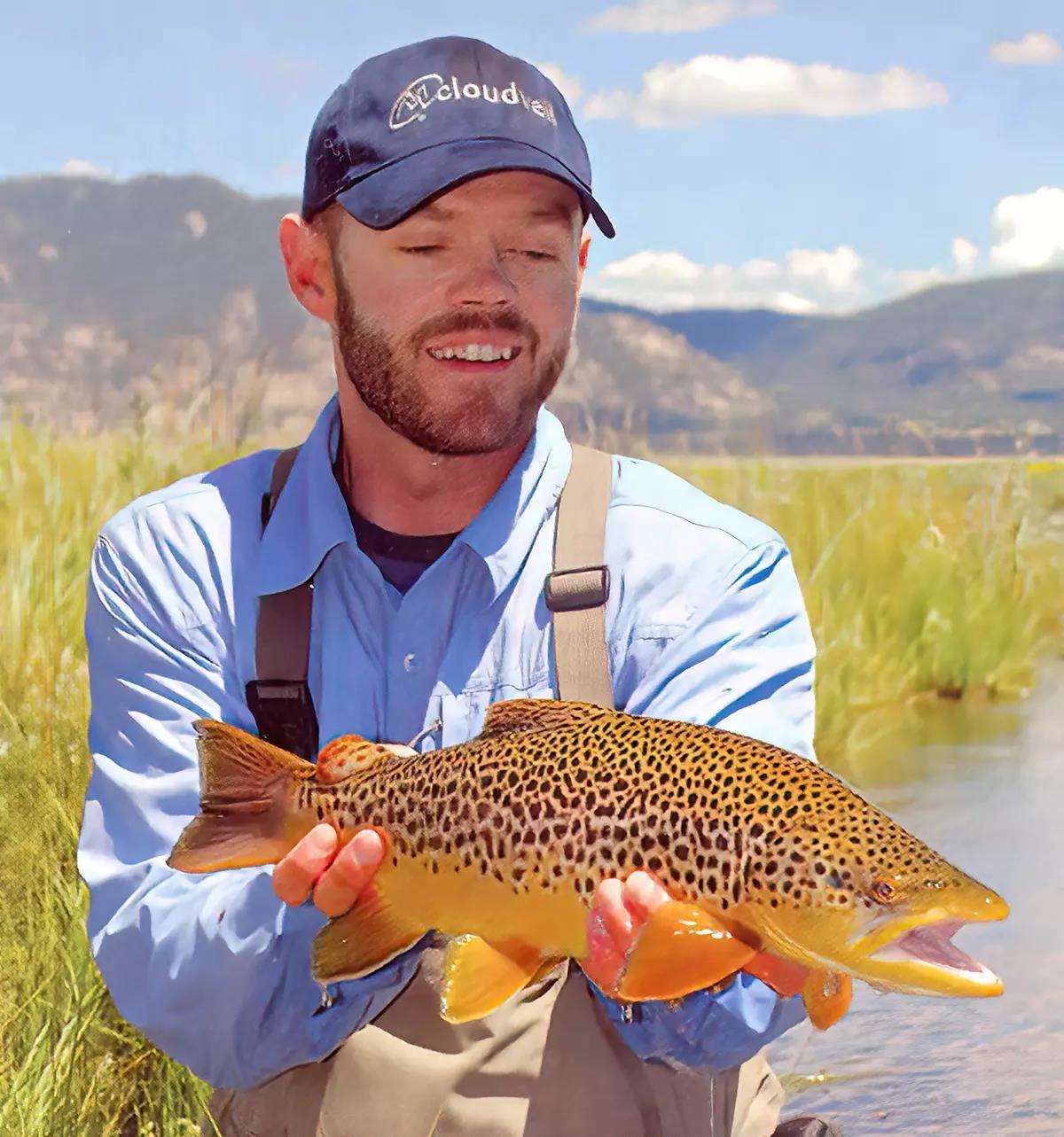 Fly angler Landon Mayer kneels in a stream holding a good-sized brown trout. 