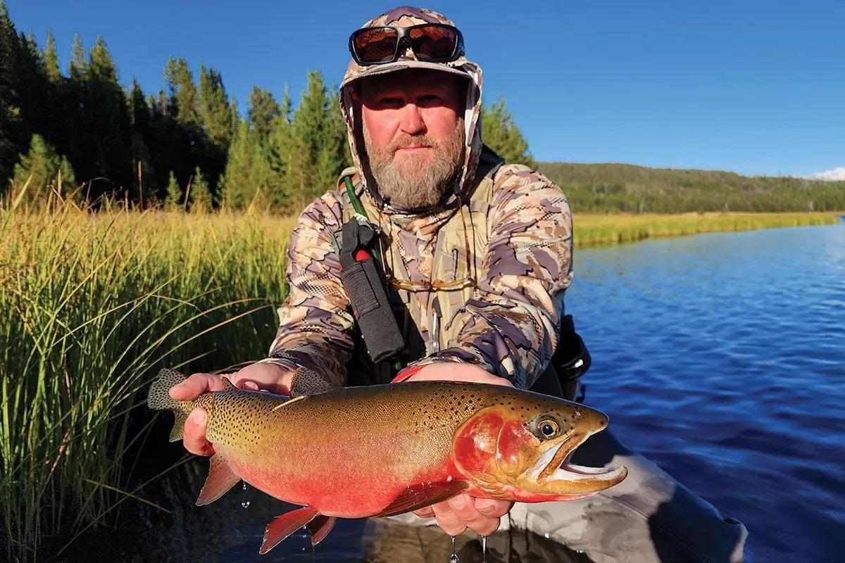 A fly angler holding a brightly colored westslope cutthroat trout in a lake.