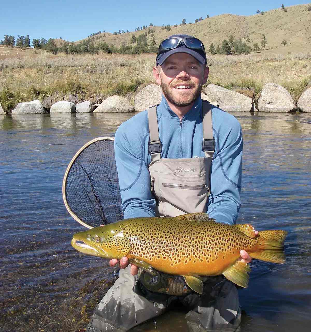 Fly angler Landon Mayer holds an obese and long brown trout just above the water's surface.