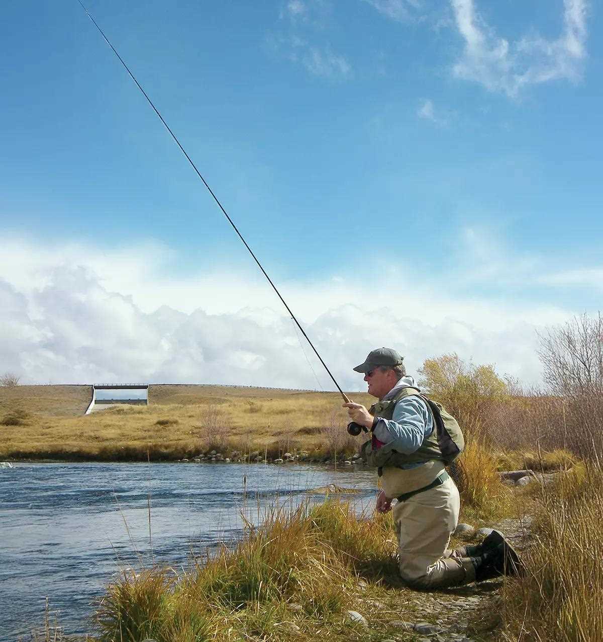 A fly angler kneeling next to a stream, high-stick nymphing. 