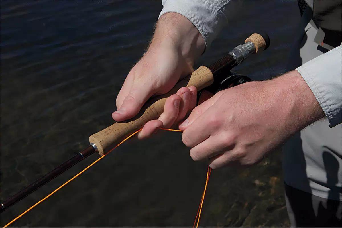A man's hands holding a fly rod, demonstrating a fly retrieve.