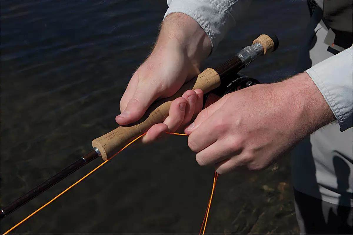 A man's hands holding a fly rod, demonstrating a fly retrieve.