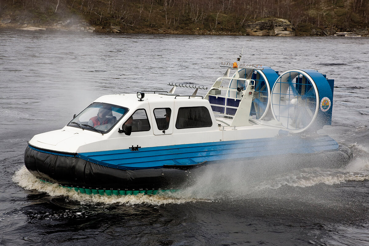 A large covered white, blue, and black hovercraft cruising over water