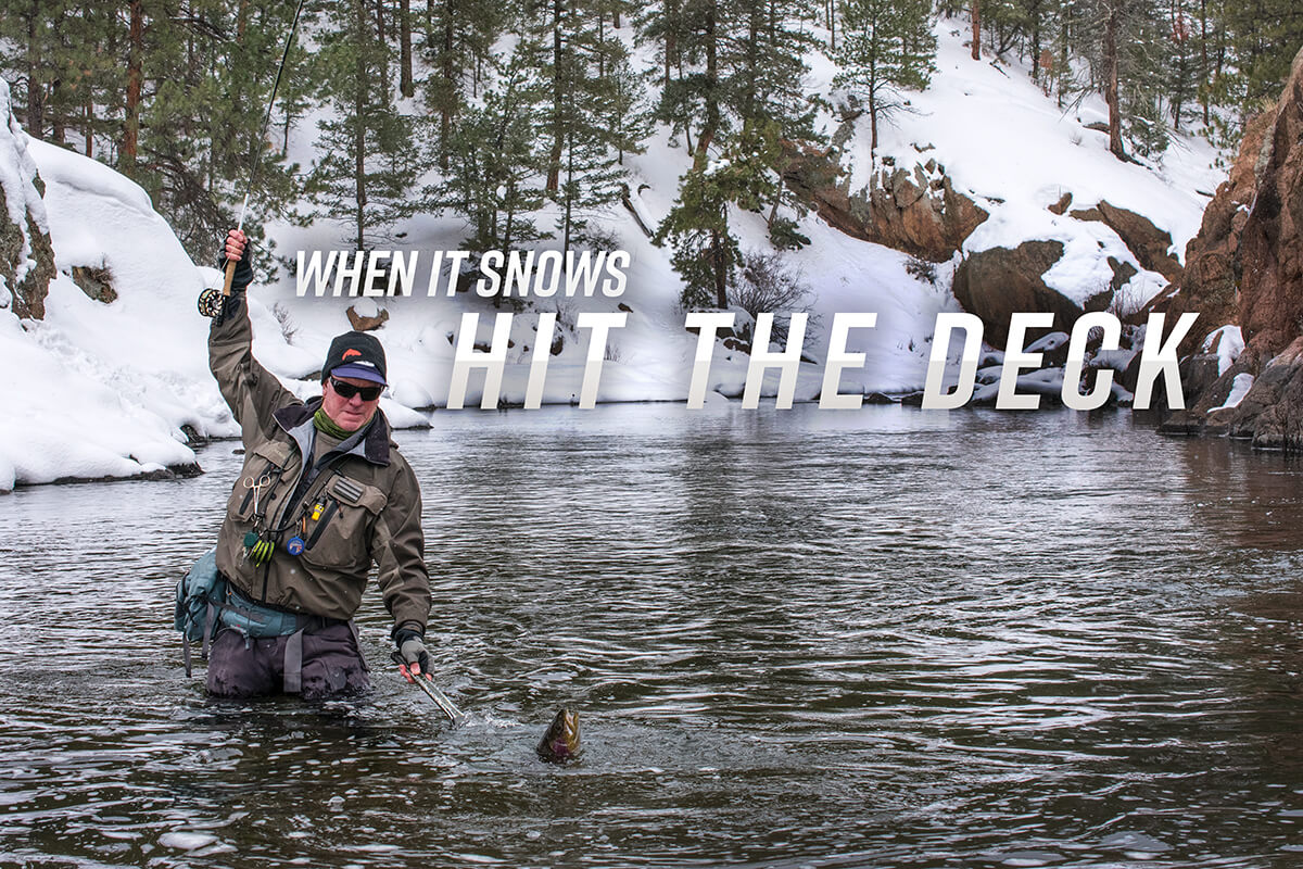 A fly angler fighting and landing a large trout in a snowy river canyon; South Platte River, Colorado. 