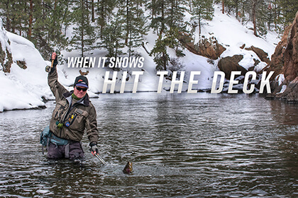 A fly angler fighting and landing a large trout in a snowy river canyon; South Platte River, Colorado. 